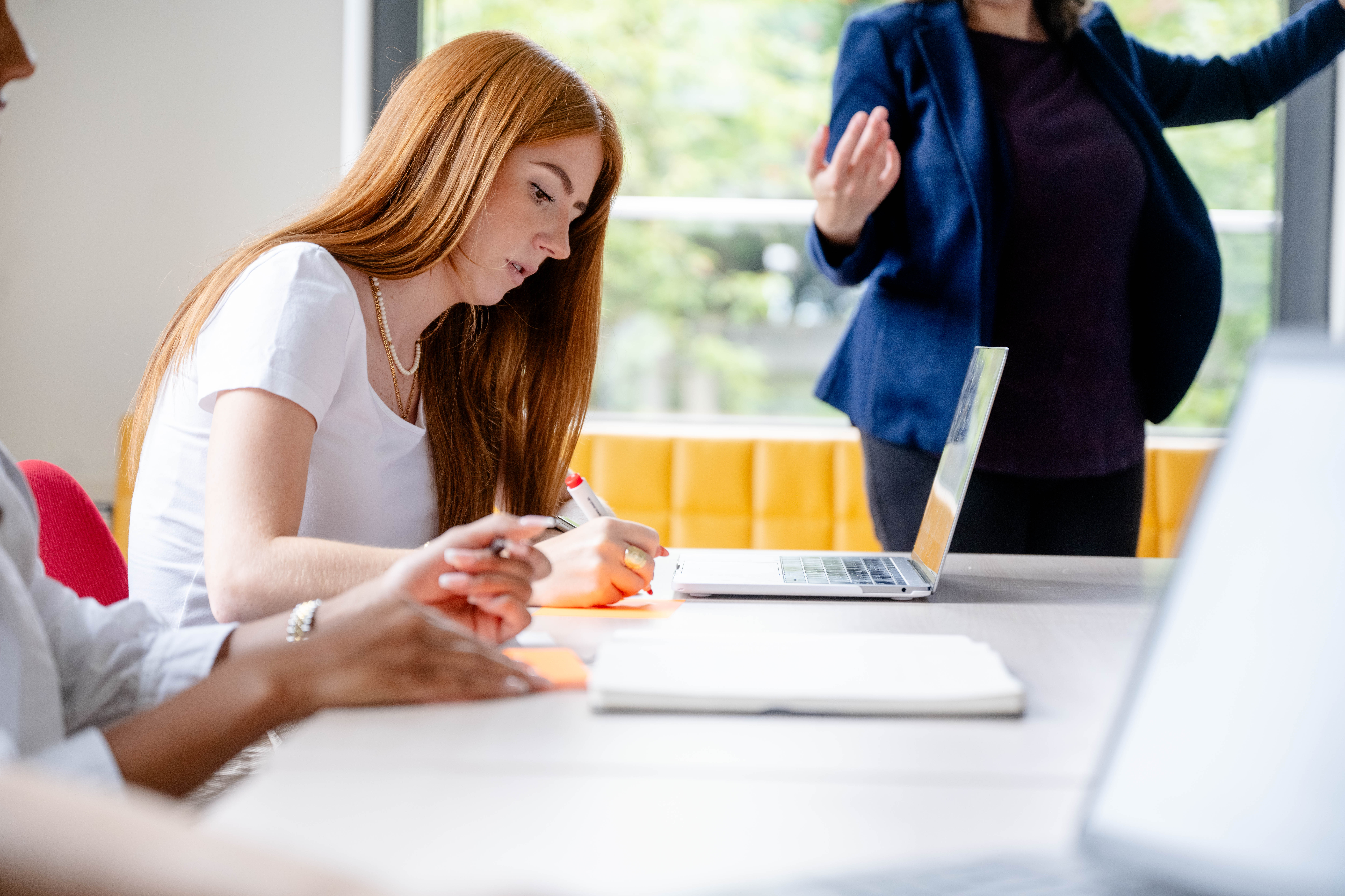 Das Bild zeigt eine junge Frau in einer Workshopsituation, vor sich ein Laptop macht sie Notizen, hinten schemenhaft die Vortragende.