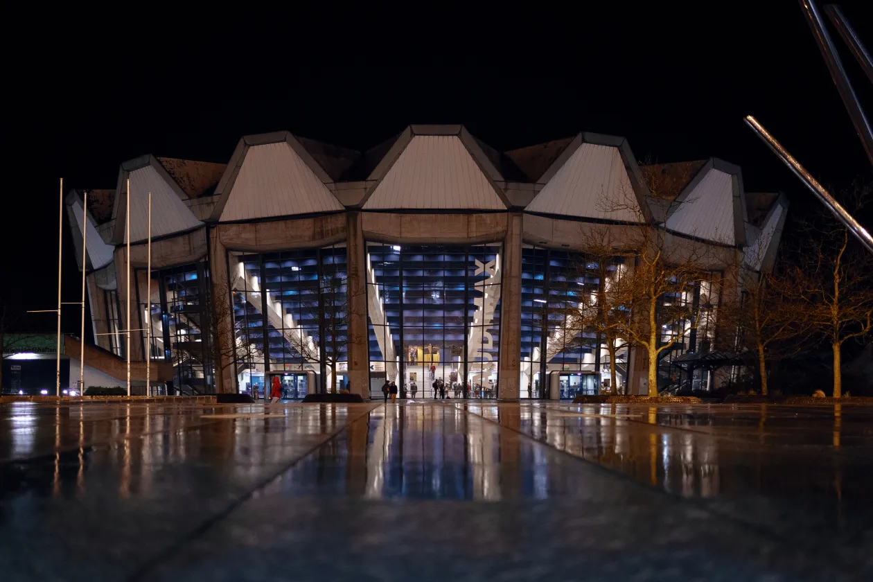 Das helle erleuchtete Audimax im Dunklen, Personen gehen darauf zu.