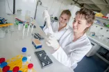 Zwei Forscherinnen im weißen Kitteln führen ein Experiment im Labor durch.