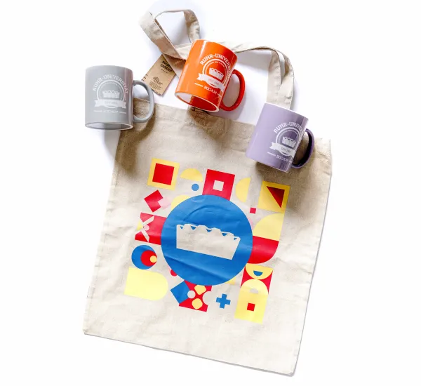Jubiläumsedition des Unishops: ein Baumwollbeutel und drei Becher in verschiedenen Farben mit Audimaxprint